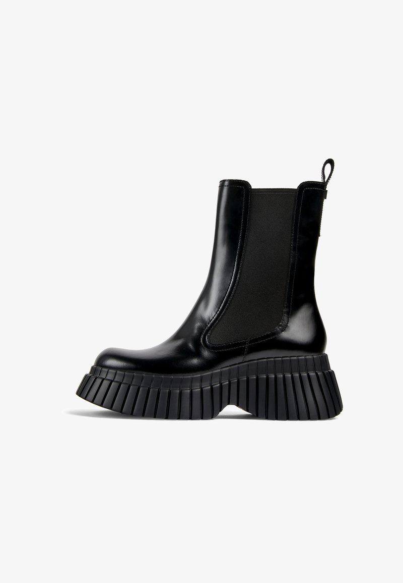 Botas negras hasta el tobillo con un acabado brillante, paneles laterales elásticos, suela de plataforma gruesa acanalada y tirador en la parte posterior para facilitar el calzado.