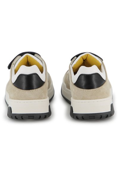 Paire de baskets en daim beige avec des empiècements noirs au talon, des semelles intermédiaires blanches et des intérieurs rembourrés jaunes, vue de dos sur fond blanc.