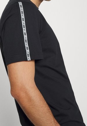 Schwarzes T-Shirt mit kurzen Ärmeln aus Baumwolle, mit einem grauen Nike-Logo-Tape entlang der Schulternaht. Einfaches, klassisches Design.