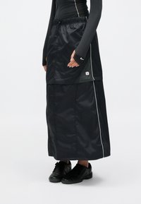 Μαύρη επενδεδυμένη φούστα με κομψό, αδιάβροχο ύφασμα, με λευκή επένδυση και ελαστική μέση, συνδυασμένη με μαύρα αθλητικά παπούτσια.