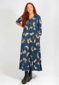 Langes Kleid aus marineblauem Stoff mit einem durchgehenden Tigerprint. Vorn mit Knöpfen, langen Ärmeln und seitlichen Taschen. Getragen mit schwarzen Schnürstiefeln.