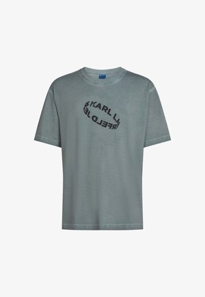 Valkoinen tee-paita, jossa on rento leikkaus. Rintanyöriin on painettu musta soikea logo, jossa lukee "KARL LAGERFELD". Lyhyet hihat.