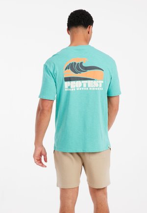 Turkis kortærmet t-shirt med et bølgedesign og logo på ryggen. Blødt stof med en afslappet pasform. Shortsene er lys beige.