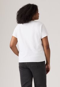 White cotton t-shirt with short sleeves, round neckline, and a relaxed fit. Worn with dark gray jeans, viewed from the back.