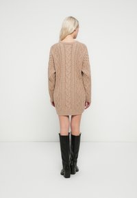 Knit sweater dress in light beige with cable patterns, long sleeves, and ribbed hem. Paired with knee-high black boots.