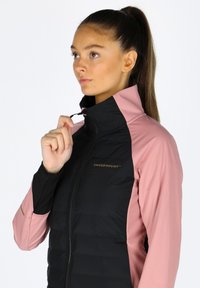 Schwarze und rosa isolierte Jacke mit hohem Kragen, Reißverschluss und Logo. Glatte Textur an den Ärmeln und gepolsterte Vorderseite für Wärme.