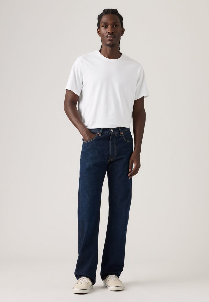 White short-sleeve t-shirt paired with dark blue straight-leg jeans, showcasing a classic design and a relaxed fit. Worn with white sneakers.