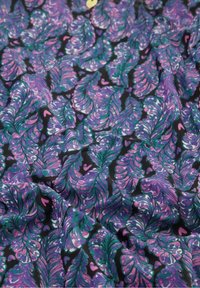 Tessuto colorato con un motivo di foglie in viola e verde acqua su uno sfondo nero, con piccoli accenti a forma di cuore rosa sparsi.