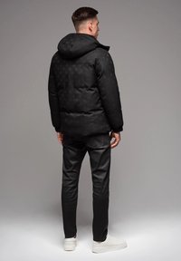 Svart puffjacka med huva som har ett texturerat mönster, ihopparat med slim-fit svarta byxor och vita sneakers.