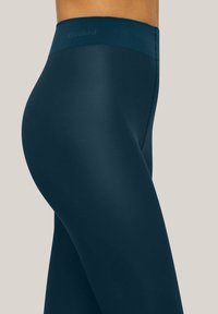 Leggings verde petrolio scuro con una texture liscia ed elastica, dotate di una fascia in vita larga con un marchio discreto. Design aderente e elegante.