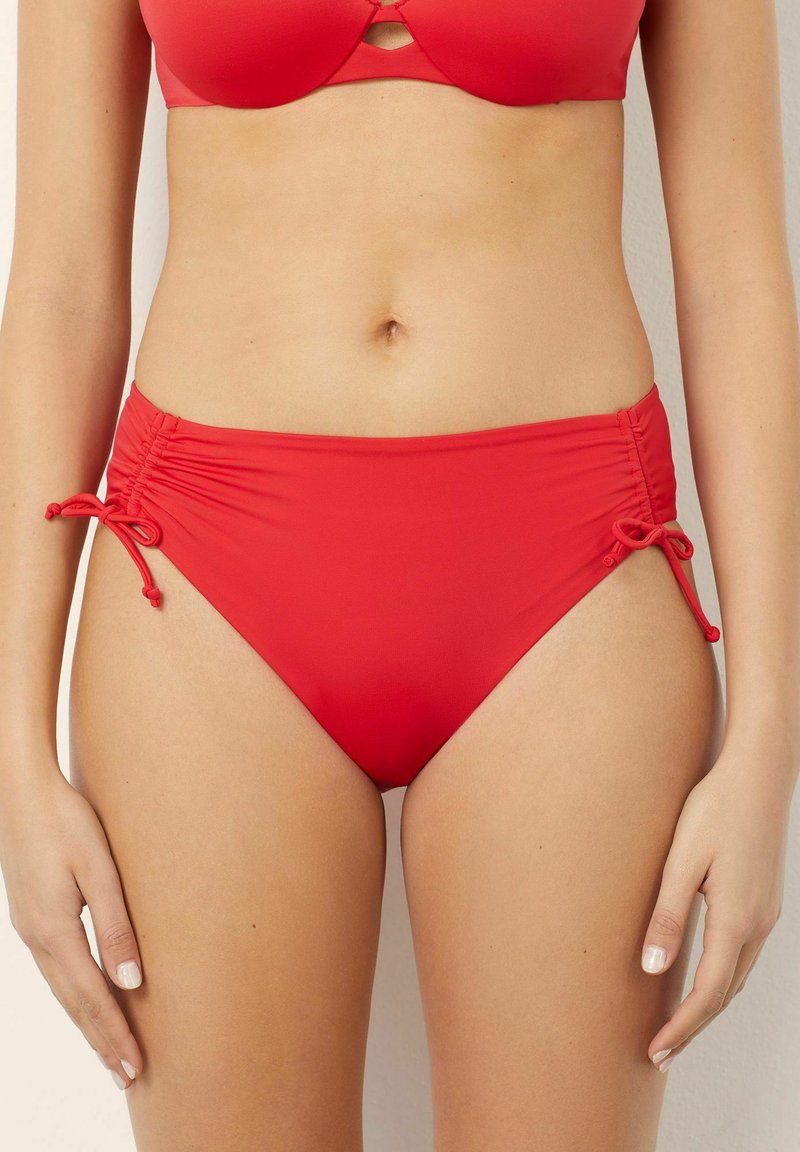 Funda de bikini roșie, confecționată dintr-un material neted. Are panouri laterale gathered și sireturi reglabile pentru o potrivire personalizată. Design cu talie medie.