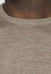 Beżowa dzianinowa tkanina swetra o fakturze, z prążkowanym dekoltem, posiadająca subtelny melanżowy wzór. Materiał wydaje się miękki i elastyczny.