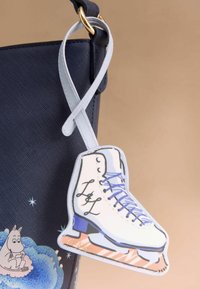 Námořnická kabelka s texturovaným materiálem, která obsahuje charm v podobě bílého kluzáku na led se modrými akcenty a tkaničkami, připevněný světle modrým popruhem.