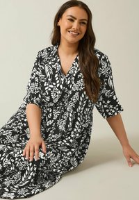 Schwarzes Kleid mit weißem floralen Muster, V-Ausschnitt, kurzen Ärmeln und elastischer Taille. Glatter Stoff mit sanftem Fall, knielanger Rock.