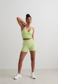 Lichtgroene sportbeha en shortset in een aansluitend ontwerp, gemaakt van elastisch materiaal, gecombineerd met witte sportschoenen.
