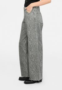 Grijs denim wijde broek met luipaardprint en rafelige zoomdetails. Heeft een hoge taille en zijzakken, aangevuld met zwarte schoeisel.
