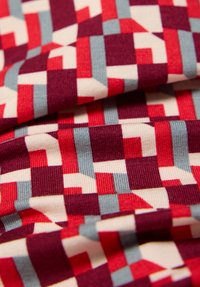 Mehrfarbiger Stoff mit einem geometrischen Muster aus roten, weißen und blauen Blöcken und einer strukturierten Strickoberfläche. Weiches, flexibles Material.