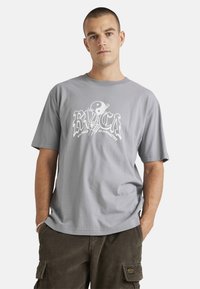 Gray cotton t-shirt featuring a white graphic logo with "RVCA" and "balance of opposites" text. Short sleeves, relaxed fit.