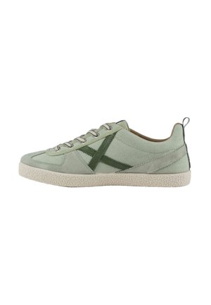 Zapatilla baja verde claro con suela beige texturizada, detalle lateral en X verde oscuro y cordones a juego, vista desde el lado exterior.