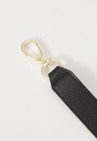 Fermoir pivotant en métal doré fixé à une sangle en cuir noir texturé avec des coutures détaillées sur fond blanc.