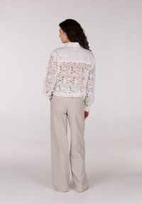 Witte kanten blouse met bloemenpatroon, lange mouwen en een cropped ontwerp. Gecombineerd met lichtbeige, wijde broekspijpen. Minimalistische stijl.