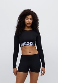 Must pikkade varrukatega lühike pluus, millel on kontrastne valge "DIESEL" logo paelal, sobitunud mustade lühikeste pükstega, mõlemad sileda kangaga.