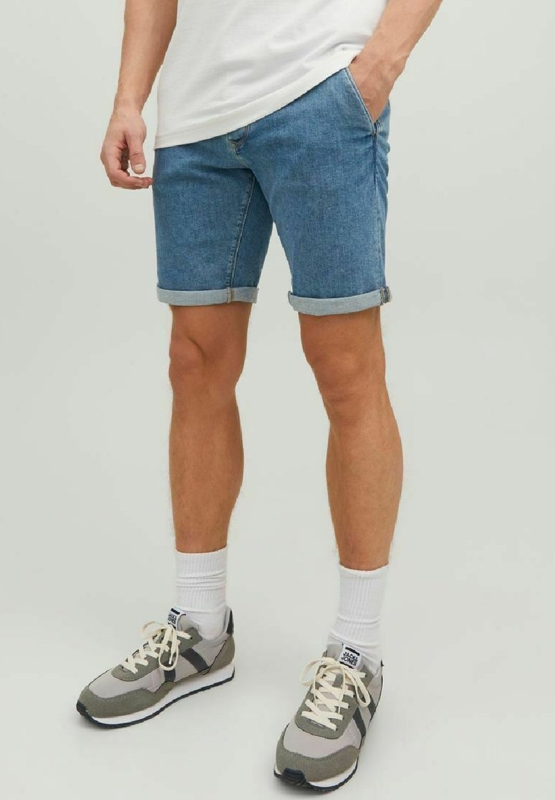 Bermudas de mezclilla azul claro con dobladillos enrollados, usadas con zapatillas deportivas grises y blancas y calcetas blancas. Diseño simple con corte recto.