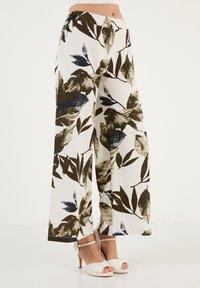 Wijdvallende broek van een lichtgewicht materiaal met een witte achtergrond en grote groene, marineblauwe en zwarte bladvormen; heeft een ontspannen pasvorm.