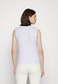 Top branco sem mangas com um decote redondo, design ajustado e textura suave. Vista pela parte de trás, combinado com calças brancas.