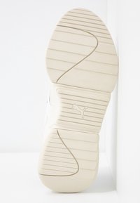 Suola di sneaker Puma di colore crema, in gomma testurizzata con scanalature orizzontali e diagonali, che presenta un piccolo logo impresso.