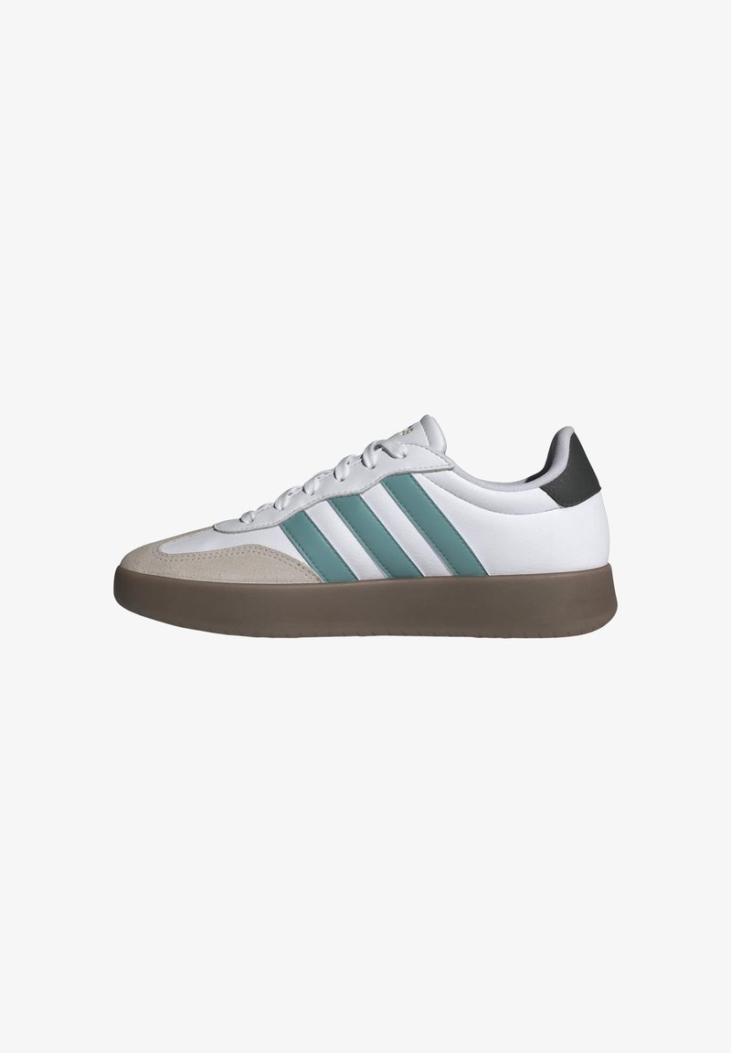 Zapatillas deportivas blancas con rayas turquesa, puntera de ante y suela de goma marrón. Textura suave, diseño de cordones y tacón mínimo.
