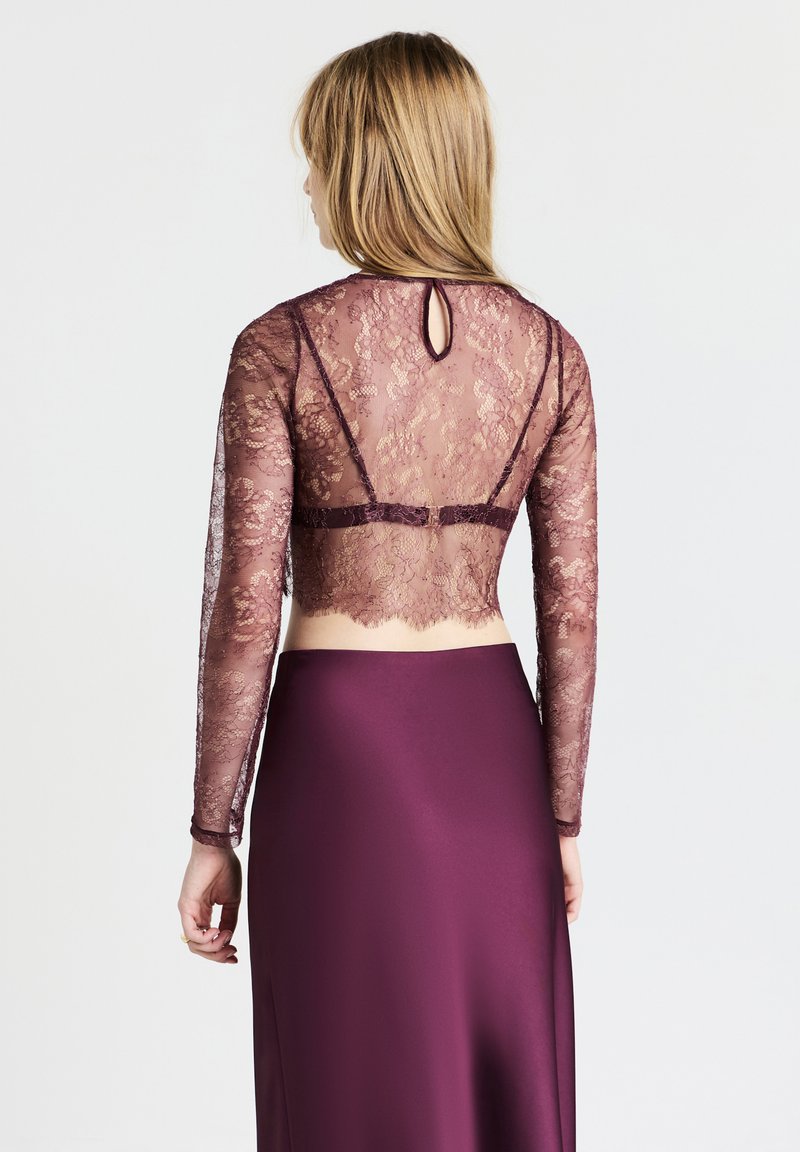 Top in pizzo a maniche lunghe color malva, con un motivo floreale in rilievo, abbinato a una gonna fluida burdeos a tinta unita. Dettaglio di chiusura a forma di chiave sul retro visibile.