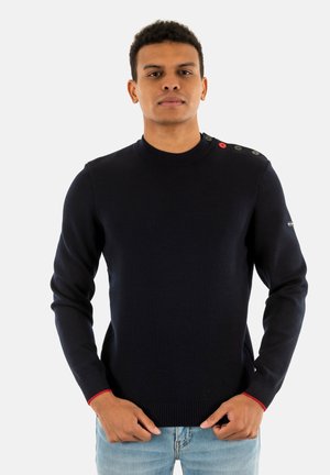 Maglione blu navy a maglia con collo alto, dotato di quattro bottoni sulla spalla e accenti rossi sui polsini. Texture morbida, design aderente.