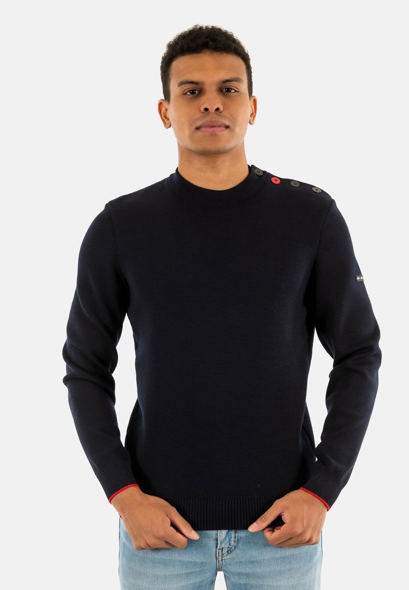 Maglione blu navy a maglia con collo alto, dotato di quattro bottoni sulla spalla e accenti rossi sui polsini. Texture morbida, design aderente.