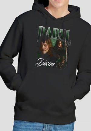 Person trägt schwarzen Hoodie mit grünem und weißem Grafikdruck, der drei Bilder eines Mannes zeigt, der einen Stab hält, und den Text "Daryl Dixon".