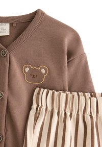 Cardigan marrone con ricamo di orso, caratterizzato da chiusure a bottone, abbinato a pantaloni a righe crema e marrone. Texture del tessuto liscia.
