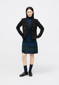 Črn blazer z zlatimi gumbi, mornarsko modra turtleneck pulover in karo krilo v zeleni in modri barvi. Črne loafer čevlje in mornarsko modre nogavice dopolnjujejo obleko.