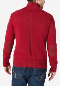 Roter Strickpullover mit hohem Kragen, gerippten Manschetten und Saum, braunen Patches an den Ellbogen und einem strukturierten Muster.