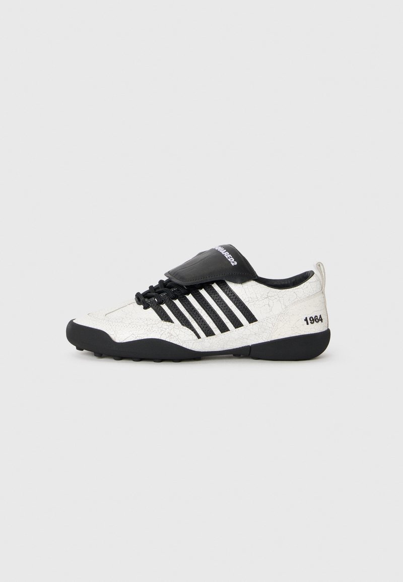 Sneaker med en vit sprucken yta, svarta accenter, fem horisontella ränder och en svart vadderad tunga med texten "1984." Svart gummisula.