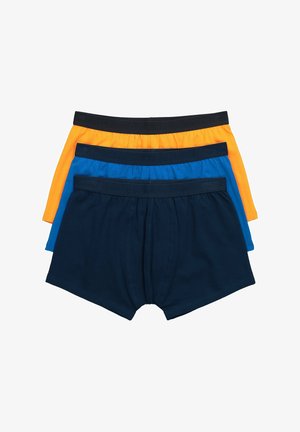 Mandoverkrop iført blå boxershorts med sort linning og svag branding, stående mod en ensartet lys baggrund.