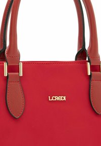 Rote Handtasche mit glatter Textur, goldenen Hardware-Details, zwei stabilen Griffen und einem Logo, das auf der Vorderseite geprägt ist.
