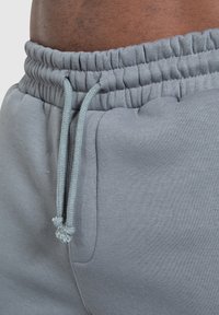 Los pantalones jogger de algodón gris cuentan con una cintura elástica con cordón, dos bolsillos laterales y una textura suave y lisa.