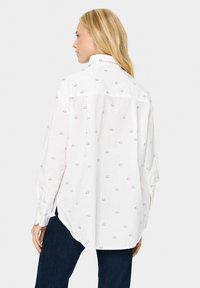 Witte lange mouwen shirt met zwarte wolkpatronen, ontspannen pasvorm, afgeronde zoom en knoopmanchetten, gecombineerd met donkerblauwe denim.