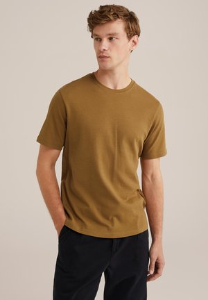 Khaki Kurzarm-T-Shirt aus weicher Baumwolle mit Rundhalsausschnitt. Lockere Passform mit glatter Textur, getragen mit dunklen Hosen.