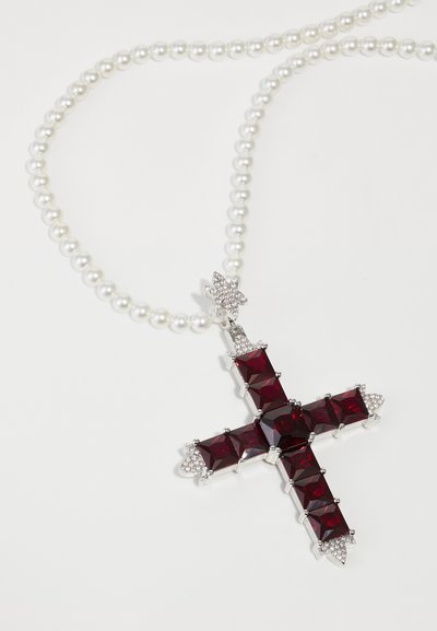 Collier en perles avec un grand pendentif en croix en pierre précieuse rouge, rehaussé de strass clairs et d'un cadre en métal argenté.