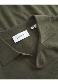 Olive green knit polo shirt featuring a classic collar, tag with "LES DEUX," and soft texture. Size label shows "M." Simple and casual design.