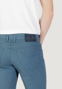Vaqueros de un azul claro con una textura suave, que presentan un parche de cuero negro con la marca y un detallado cosido en los bolsillos traseros.