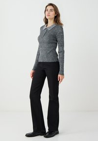 Top grigio a coste con maniche lunghe e colletto, caratterizzato da un design a maglia strutturata. Abbinato a pantaloni neri svasati e scarpe nere.