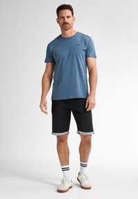 Blaues Baumwoll-T-Shirt mit kurzen Ärmeln und Rundhalsausschnitt, kombiniert mit schwarzen Denim-Shorts mit umgeschlagenem Saum und kontrastierenden Details.