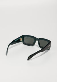 Ochelari de soare cu tentă verde, având un cadru chunky, rectangular, cu un side texturat și accente de culoare aurie pe balamale.